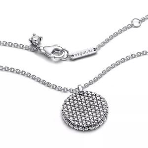 A silver Pandora necklace with a round, sparkling pendant and a branded tag near the clasp, featuring a lobster clasp closure.