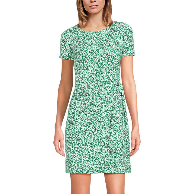 A green, short-sleeve, wrap-style mini dress with a white floral print. The dress features a round neckline and a waist tie.