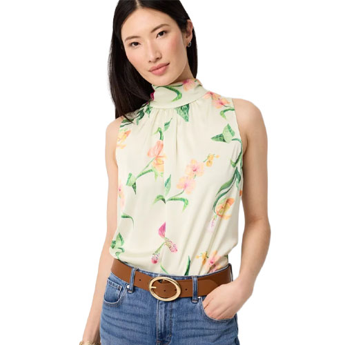A woman is wearing a sleeveless, floral-printed, high-neck blouse paired with blue jeans and a tan belt with a round buckle.