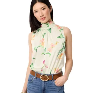 A woman is wearing a sleeveless, floral-printed, high-neck blouse paired with blue jeans and a tan belt with a round buckle.