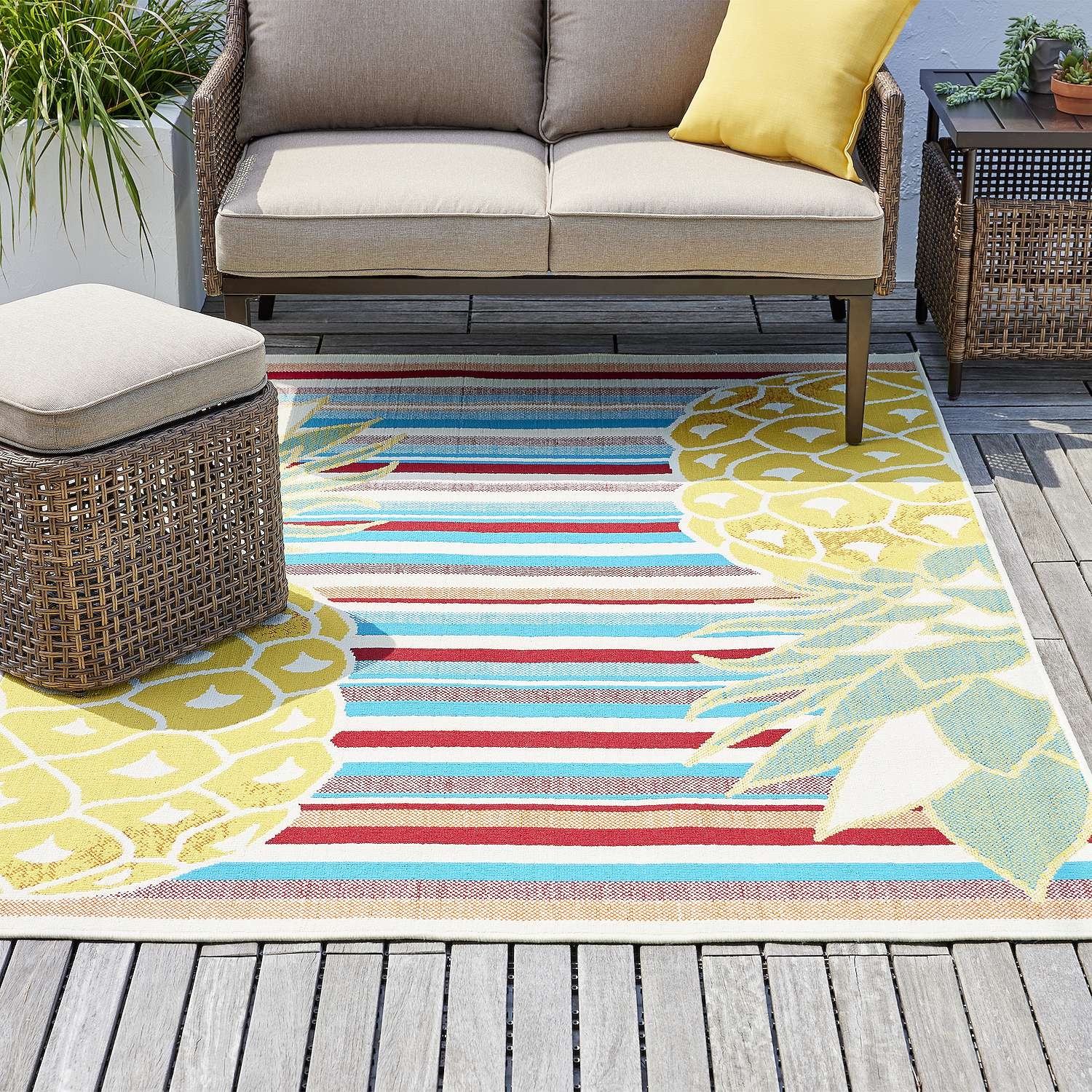 Outdoor striped rug with a floral design, accompanied by a sectional sofa and a wicker ottoman.