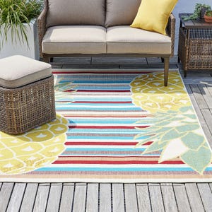 Outdoor striped rug with a floral design, accompanied by a sectional sofa and a wicker ottoman.