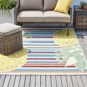 Outdoor striped rug with a floral design, accompanied by a sectional sofa and a wicker ottoman.