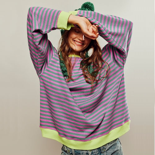 A person is wearing a green and pink striped sweater with a green bobble hat.