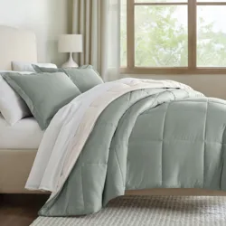 A neatly made bed features a sage green comforter set with matching pillow shams, accompanied by white and beige sheets. A bedside table with a lamp is visible, and sunlight streams through a window, creating a serene atmosphere.