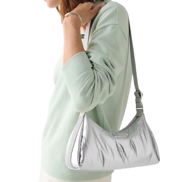A person wearing a light green sweater is carrying a silver shoulder bag with a sleek design and adjustable strap.