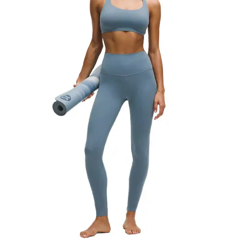 A person wearing a matching blue sports bra and high-waisted leggings holds a rolled-up yoga mat.