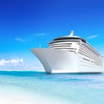 A large white cruise ship on a bright blue sea with a clear sky in the background.