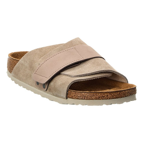A beige suede slide sandal featuring an adjustable strap and a cork footbed with a rubber sole.