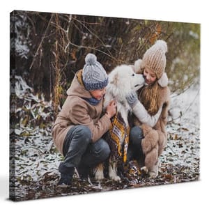 Canvas print featuring two people in winter clothing playing with a fluffy white dog in a snowy outdoor setting.