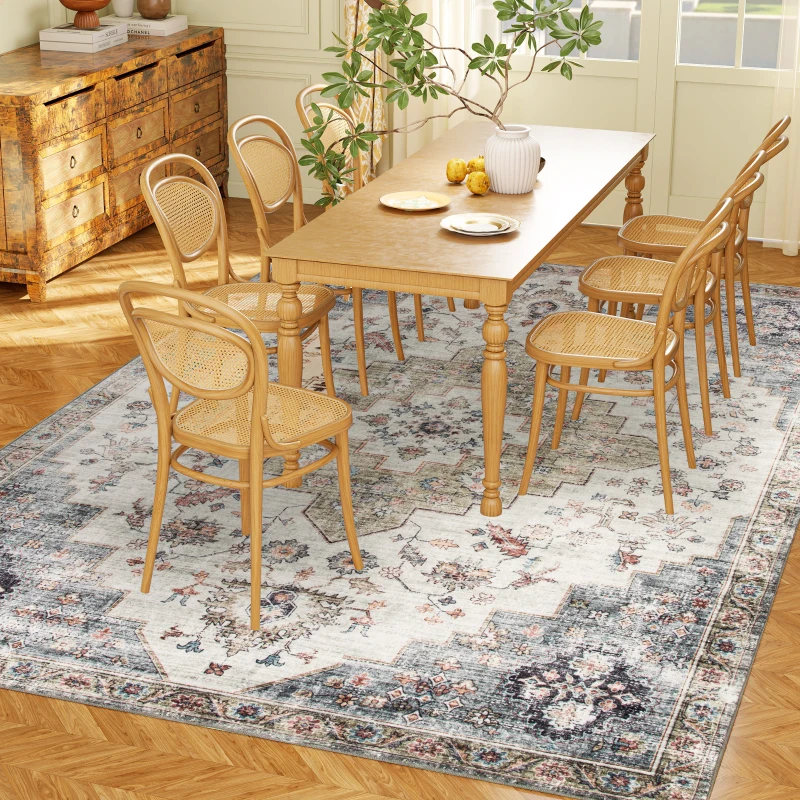A dining room setup features a wooden table with six cane-backed chairs on a decorative, floral-patterned rug. A rustic dresser and a plant in a vase add decorative elements.