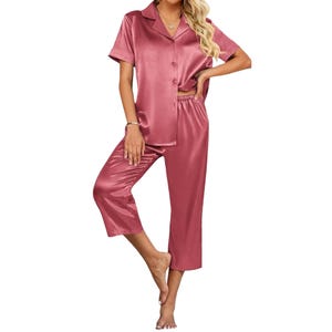 A two-piece women's satin pajama set includes a short-sleeve, button-up shirt and cropped pants in a rose-pink color, featuring a relaxed fit and shiny texture.