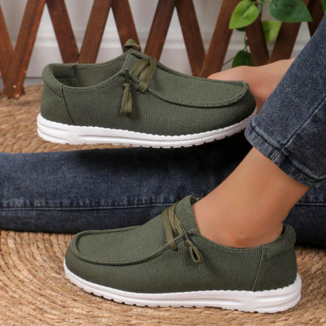 Olive green slip-on shoes with lightweight, breathable fabric and white rubber soles, featuring decorative tassel-like laces.