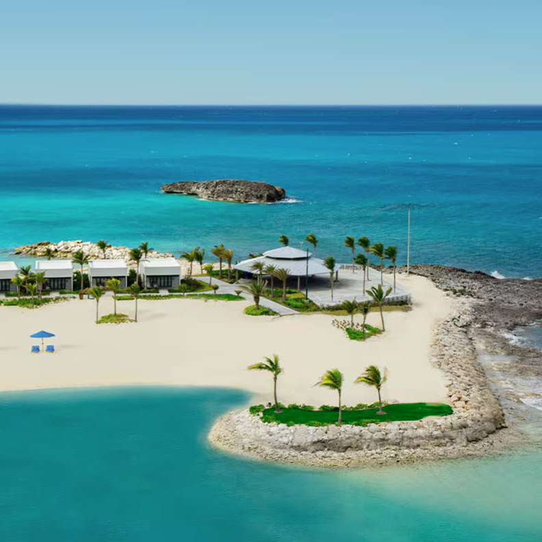 A scenic beach view features a sandy shore with beach chairs under blue umbrellas, small modern white buildings, and a pavilion surrounded by clear turquoise ocean waters and palm trees.