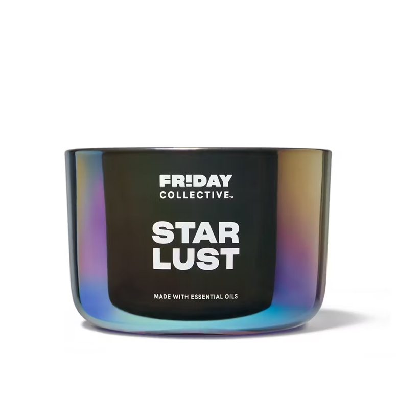 A cylindrical, iridescent glass candle labeled \“FRIDAY COLLECTIVE. STAR LUST\“ indicating it is made with essential oils.