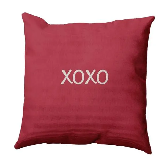 A red square pillow featuring the text \“XOXO\“ in white.