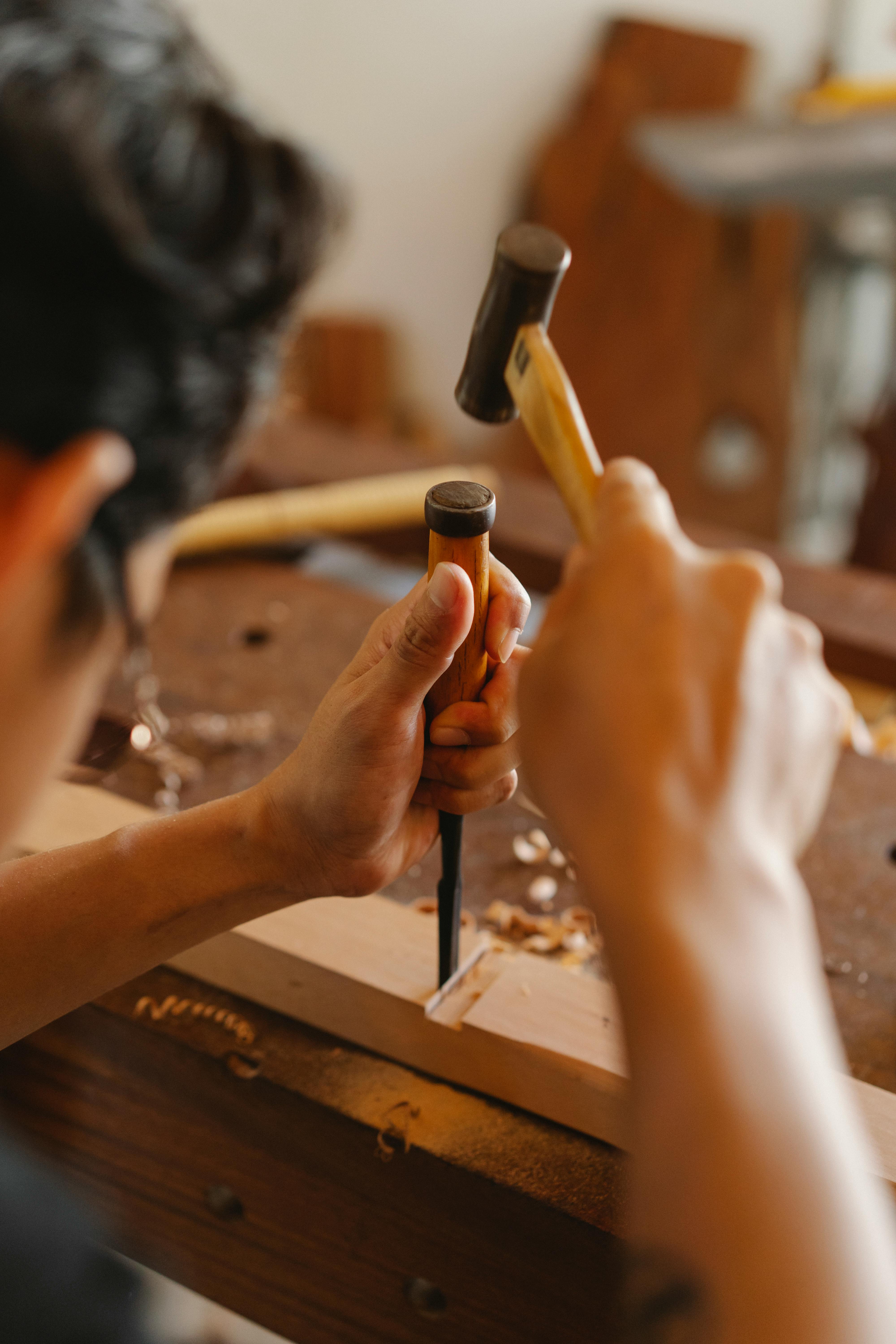 A person is using a woodworking chisel and a mallet on a wooden piece clamped to a workbench.