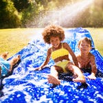 Children sliding on a blue backyard water slide on a sunny day.