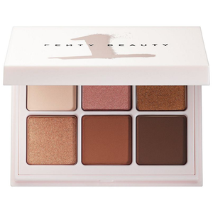 A Fenty Beauty eyeshadow palette featuring six shades: a light beige, pink shimmer, gold shimmer, bronze shimmer, matte brown, and deep brown. The packaging is white with the brand name on the lid.