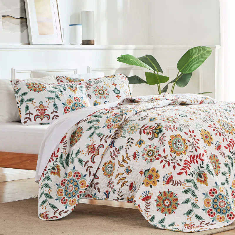 A Queen Floral Quilt Set featuring a vibrant floral pattern in red, green, yellow, and blue on a white background. Includes a quilt and matching pillow shams, adding a colorful and cozy touch to any bedroom.