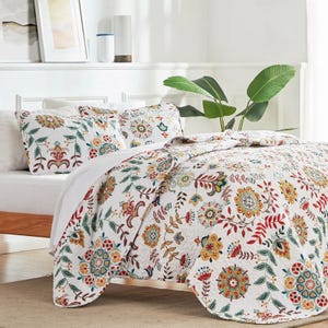 A Queen Floral Quilt Set featuring a vibrant floral pattern in red, green, yellow, and blue on a white background. Includes a quilt and matching pillow shams, adding a colorful and cozy touch to any bedroom.
