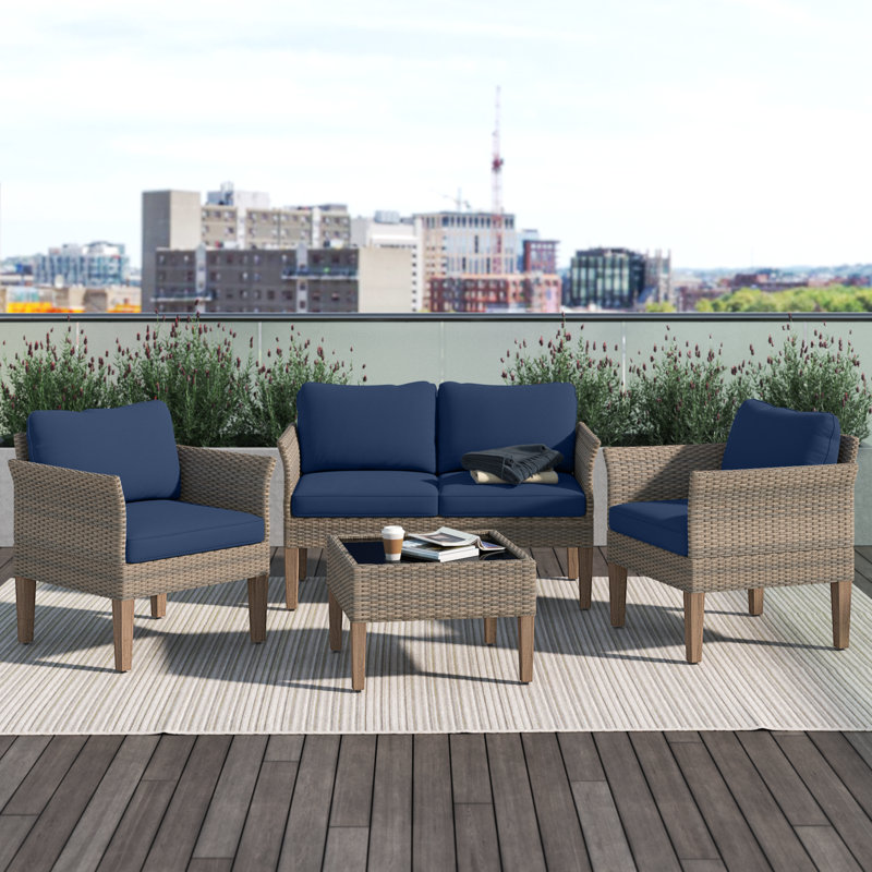 Outdoor patio set with two chairs, a loveseat, and a coffee table, featuring wicker frames and blue cushions on a rooftop deck.