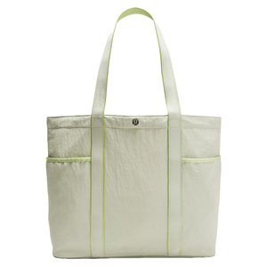 A light green tote bag with two exterior pockets and coordinating straps, featuring a round logo on the front.