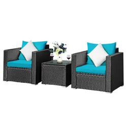 Outdoor patio furniture set with two wicker chairs and a glass-top table. Features turquoise cushions, white pillows, and holds two wine glasses and a flower vase. Set is placed on a wooden deck beside a pool.