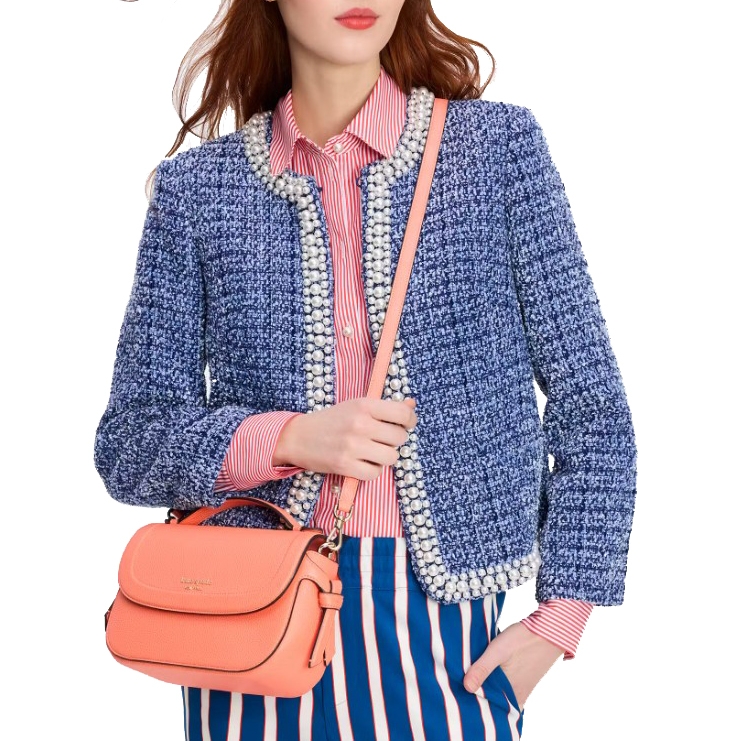 A woman wears a blue tweed jacket with pearl detailing over a red and white striped shirt and blue-striped pants, accessorized with an orange handbag.