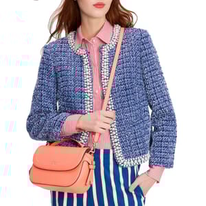 A woman wears a blue tweed jacket with pearl detailing over a red and white striped shirt and blue-striped pants, accessorized with an orange handbag.