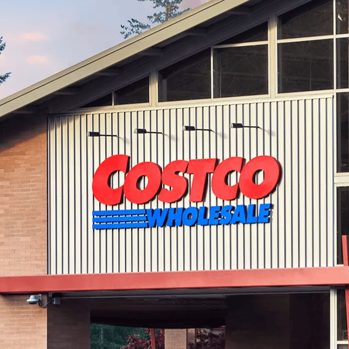 Costco Wholesale storefront featuring its recognizable red and blue logo. The building has large windows and a modern architectural design with a backdrop of trees.