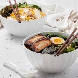 Two bowls of Asian-inspired dishes: one with ramen, pork, seaweed, and egg and the other with rice, tofu, corn, and greens.