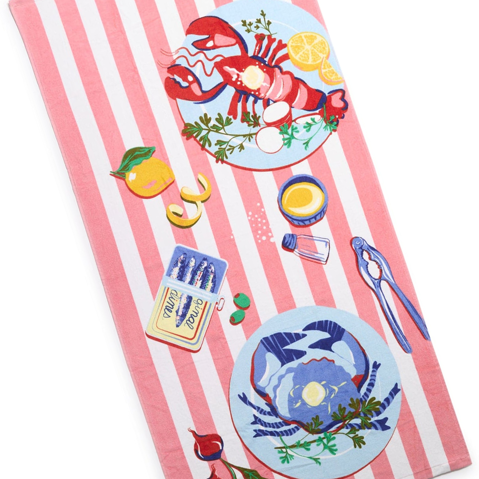 A towel with a pink and white striped pattern, featuring illustrations of a lobster, crab, lemon slices, herbs, a yellow sauce bowl, salt shaker, nutcracker, orange slice, matches, and sunglasses.