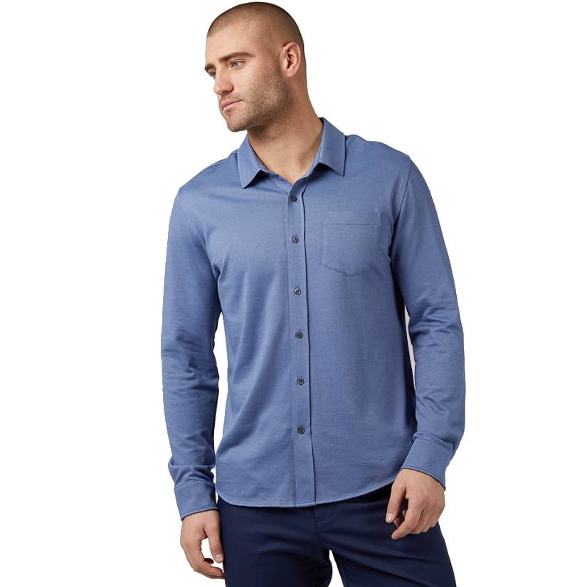 A man wears a light blue, long-sleeve, button-up casual knit shirt with a chest pocket and a spread collar, paired with dark pants.