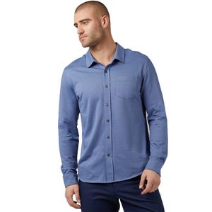 A man wears a light blue, long-sleeve, button-up casual knit shirt with a chest pocket and a spread collar, paired with dark pants.