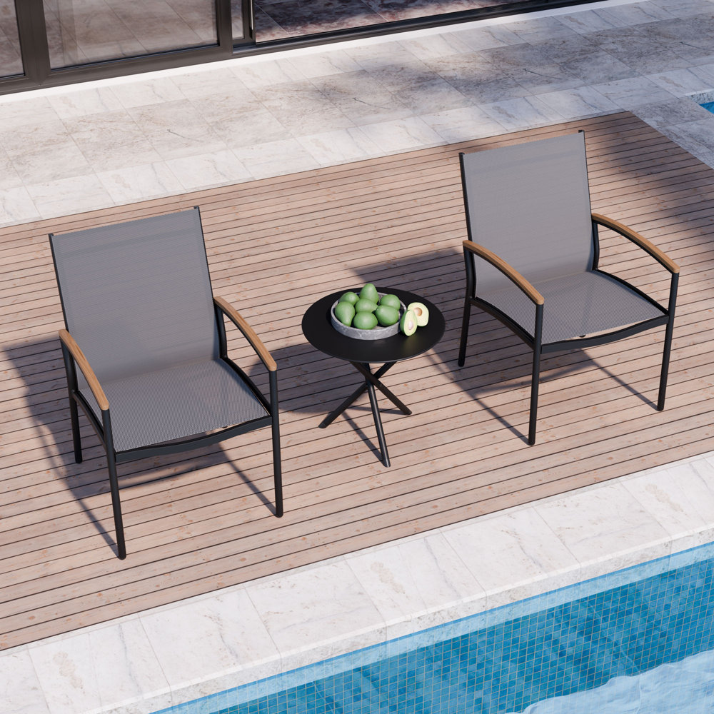 Two sling-style patio chairs with wooden armrests and a small round table, set on an outdoor deck by a pool.