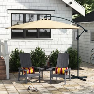 A beige cantilever umbrella with a curved black pole over two grey patio chairs with red-striped cushions and a matching small table.