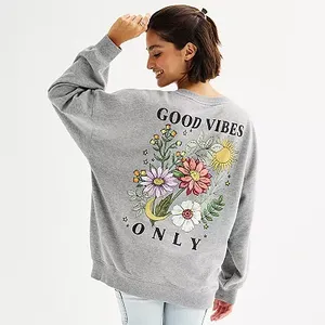 A woman wears a gray oversized sweatshirt with a colorful \“GOOD VIBES ONLY\“ floral design on the back.