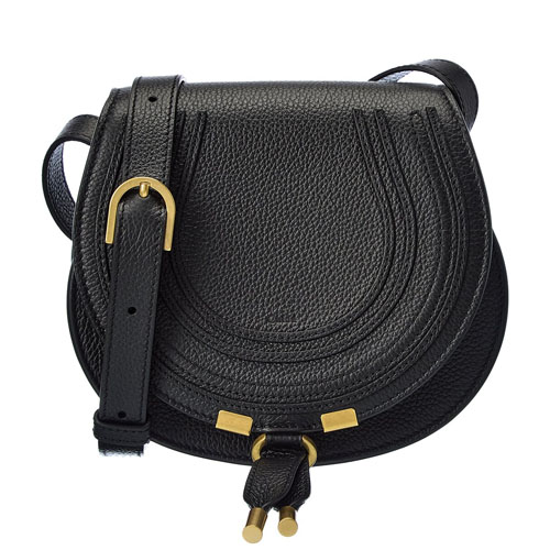 The Chloe Marcie Saddle Bag is a black, textured leather crossbody bag featuring a curved flap with stitched detailing and gold-tone hardware accents, including two dangling tassels.