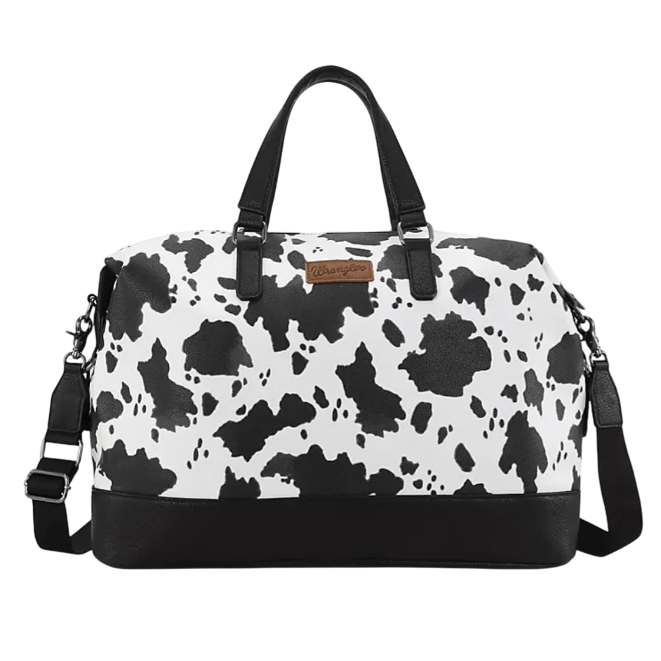 A black and white duffel bag with a cow print design, featuring black handles, a detachable shoulder strap, and a brown \“Wrangler\“ label on the front.