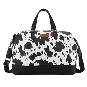 A black and white duffel bag with a cow print design, featuring black handles, a detachable shoulder strap, and a brown \“Wrangler\“ label on the front.