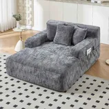 A gray, textured modular sofa with cushions, featuring built-in storage on the side armrest, is displayed in a modern living room with light wood flooring and a patterned rug.