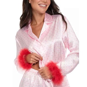 A pink satin pajama set with small polka dots, featuring long sleeves and vibrant red faux-fur trim on the cuffs.