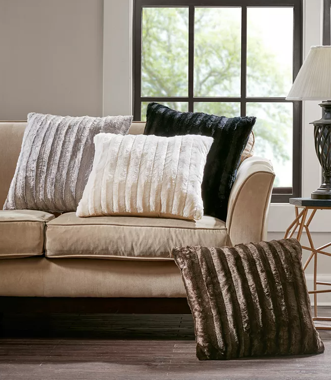 Four plush throw pillows, varying in shades of black, white, and gray, exhibit a soft, textured surface and are arranged on a beige couch.