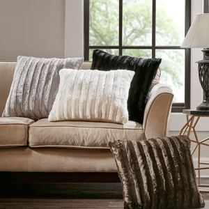 Four plush throw pillows, varying in shades of black, white, and gray, exhibit a soft, textured surface and are arranged on a beige couch.
