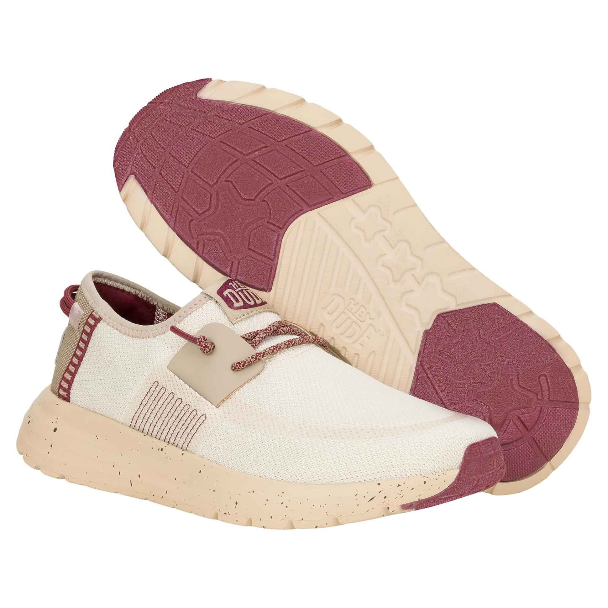 Hey Dude Women's Sirocco Shoes feature a cream and red color scheme with a textured sole for grip. They have a mesh upper for breathability, speckled midsole, and lace-up closure for a secure fit.
