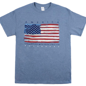 Blue t-shirt featuring a distressed-style American flag with the word \“America\“ above and \“Handcrafted with Pride Since 1776\“ below.