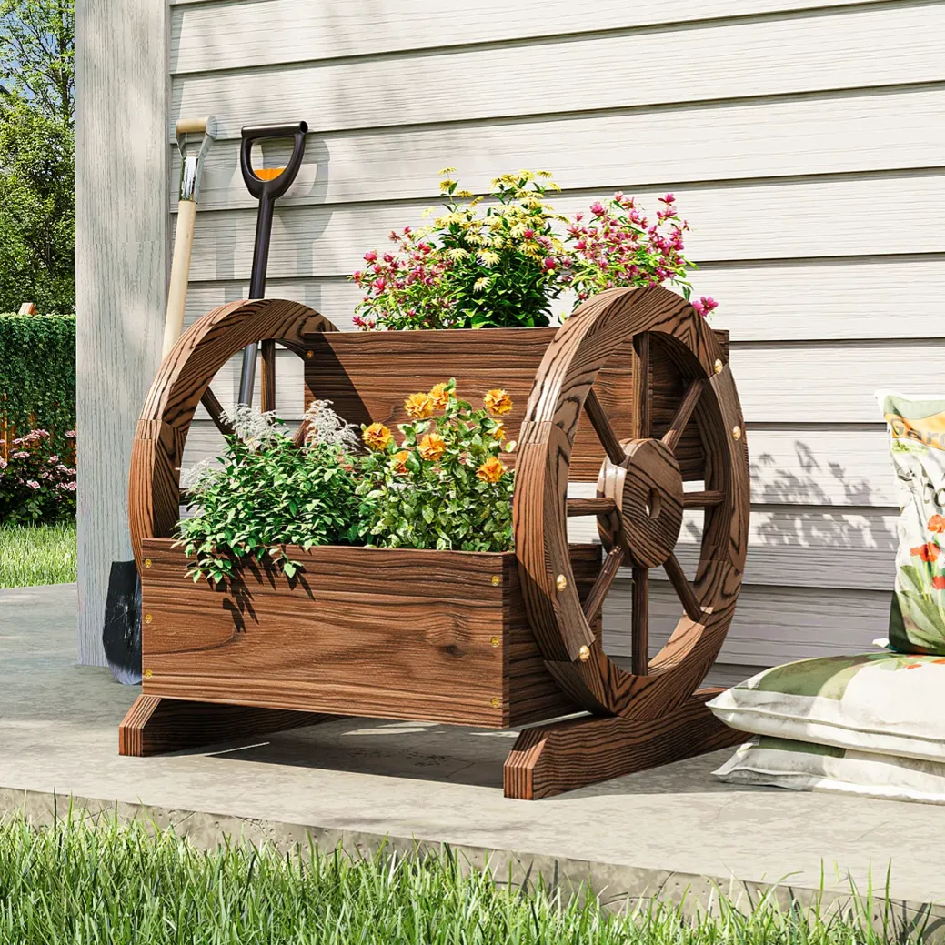 Wooden wagon wheel planter with colorful flowers on a patio, accompanied by garden tools and a decorative cushion.
