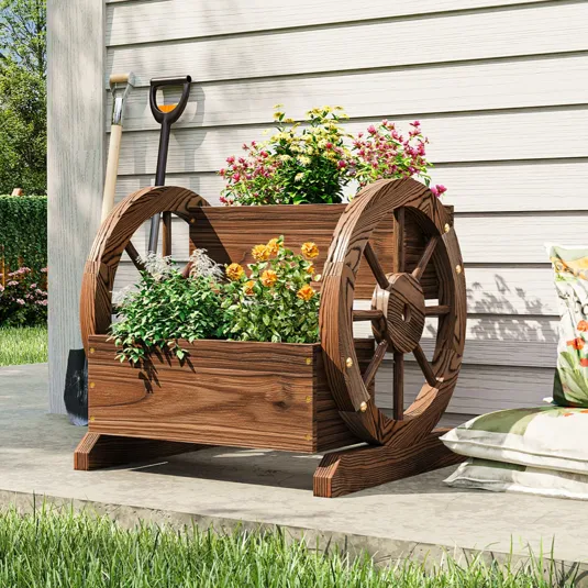 Wooden wagon wheel planter with colorful flowers on a patio, accompanied by garden tools and a decorative cushion.