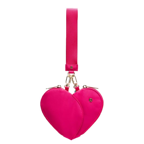 A bright pink, heart-shaped wristlet with dual zippered compartments, a gold clasp, and a detachable strap featuring the Lululemon logo.